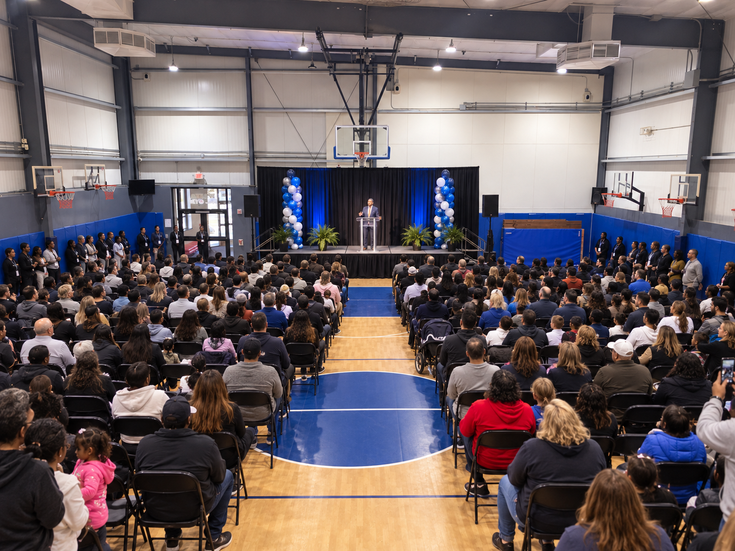 A large community event with seating and a stage inside The House of Sports gym